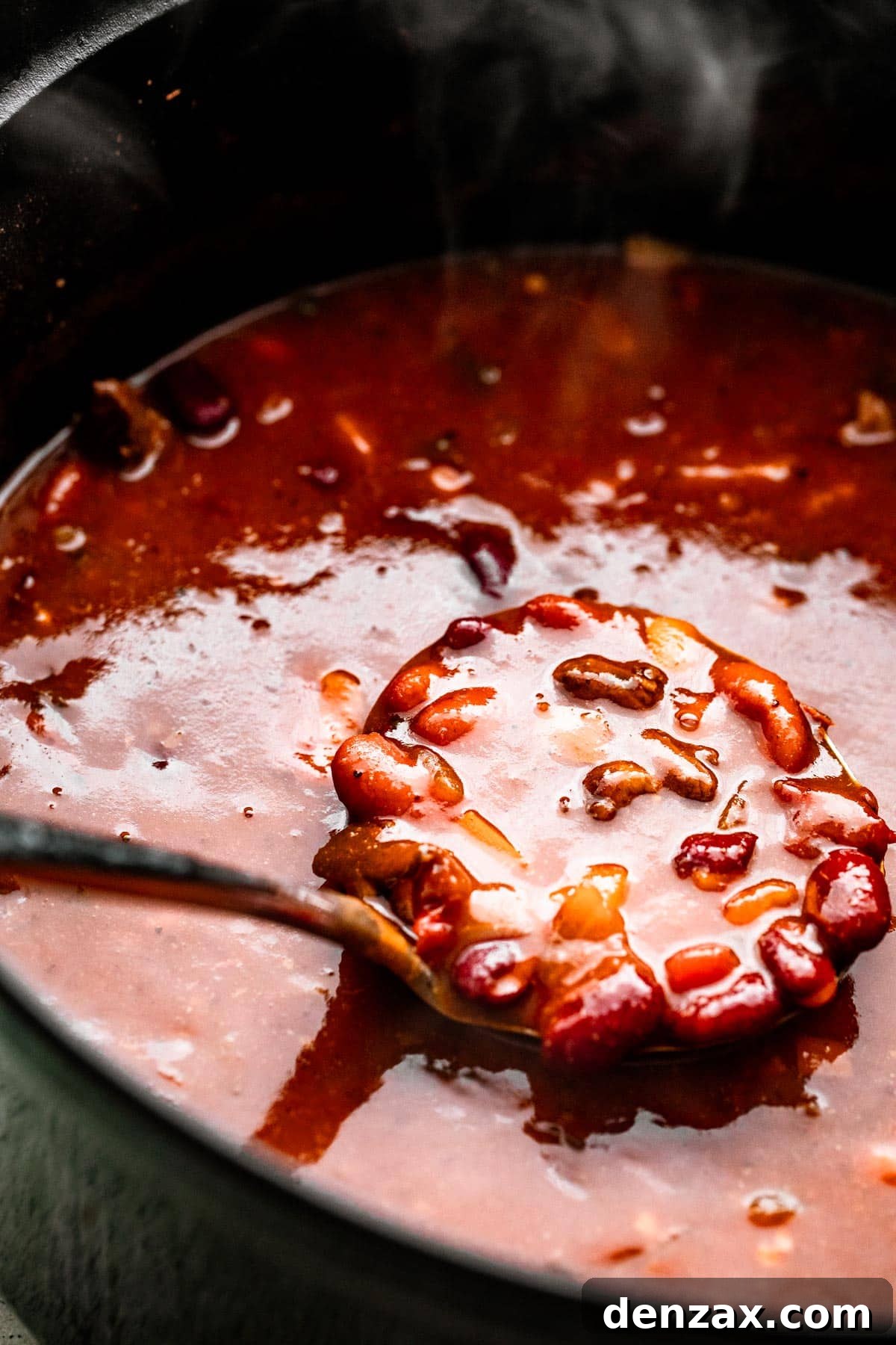 a ladle spooning out chili con carne from a dark colored pot.