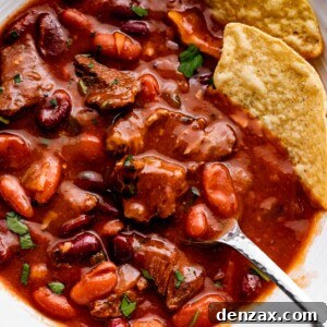 close up overhead shot of chili con carne in a white bowl, with a spoon and two tortilla chips set inside the chili