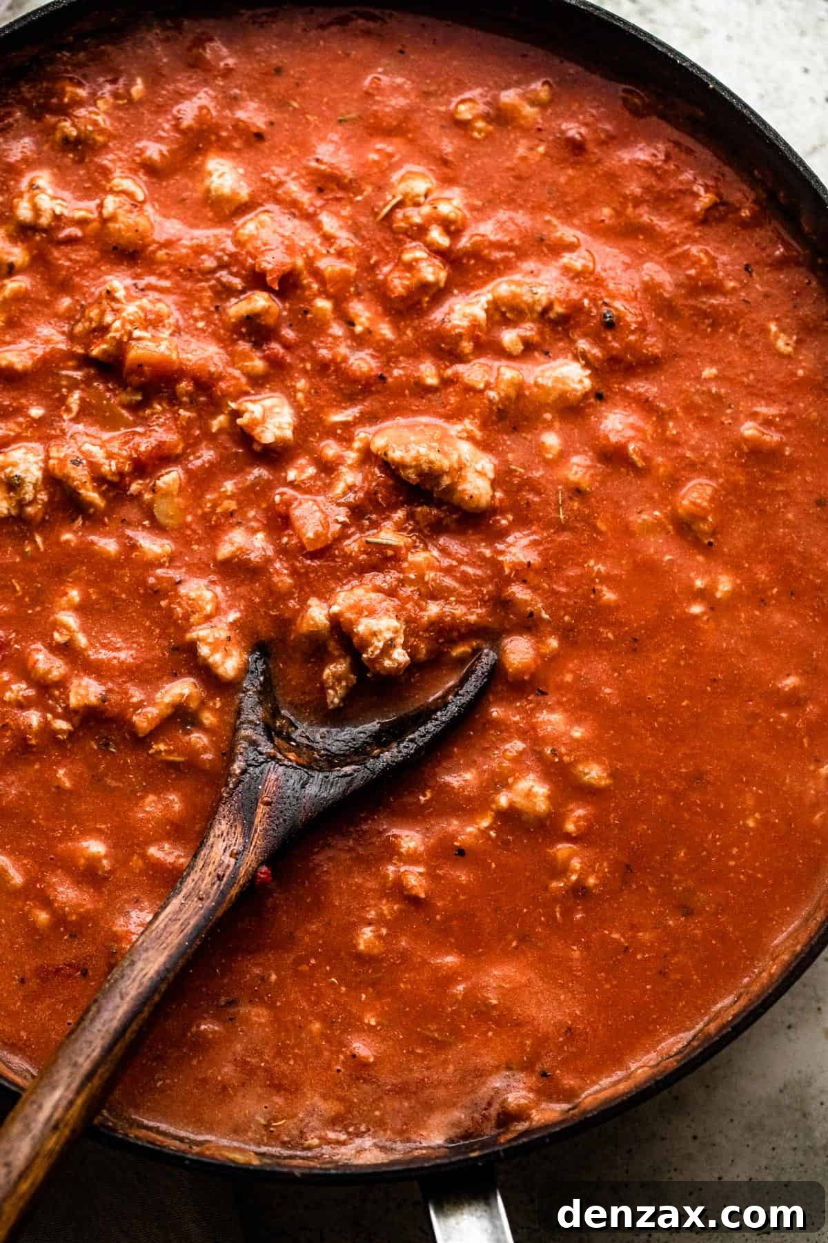 wooden spoon stirring through ground turkey in tomato sauce in a skillet.