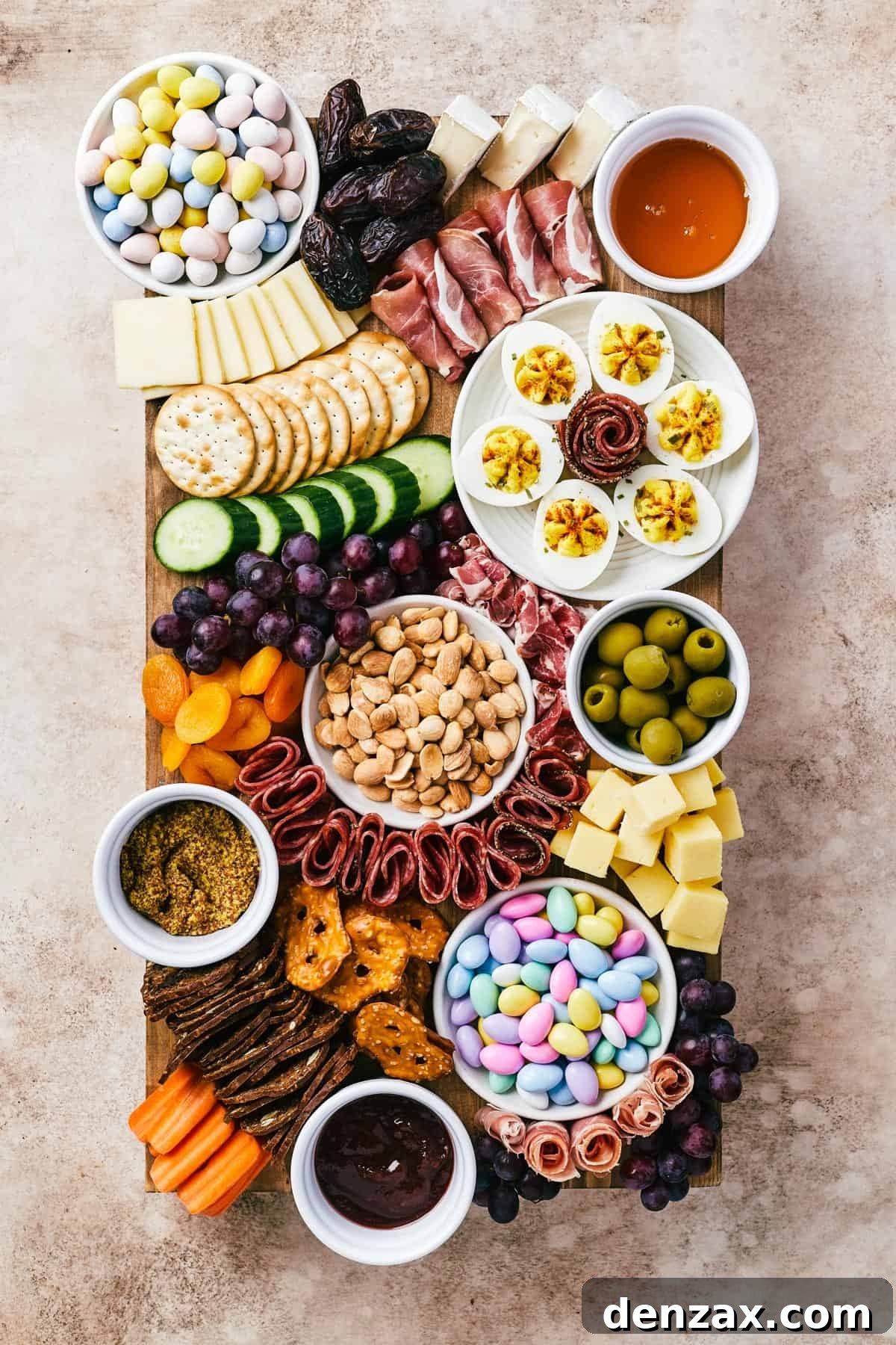 A wooden cutting board artistically arranged with meats, cheeses, crackers, olives, fruit, veggies, and more, perfect for an Easter celebration.