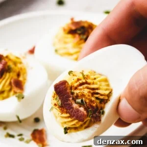 A woman's hand is lifting a deviled egg from a small plate toward the camera.