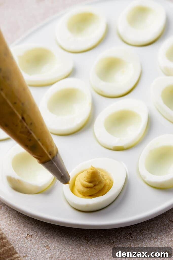 A close-up shot of a piping bag expertly filling hard-boiled egg white halves with creamy, vibrant yellow yolk mixture, creating a beautiful swirl design. This highlights the precise and artistic element of deviled egg preparation.