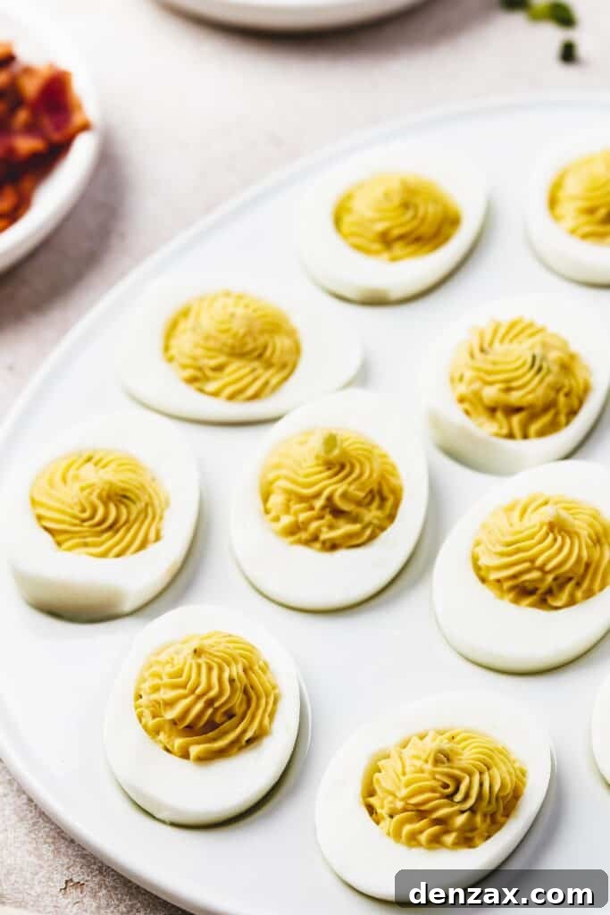 A beautifully presented egg-shaped white platter adorned with perfectly arranged deviled eggs, each garnished uniquely. Around the main platter, small, elegant bowls hold an assortment of colorful garnishes, ready for customization.