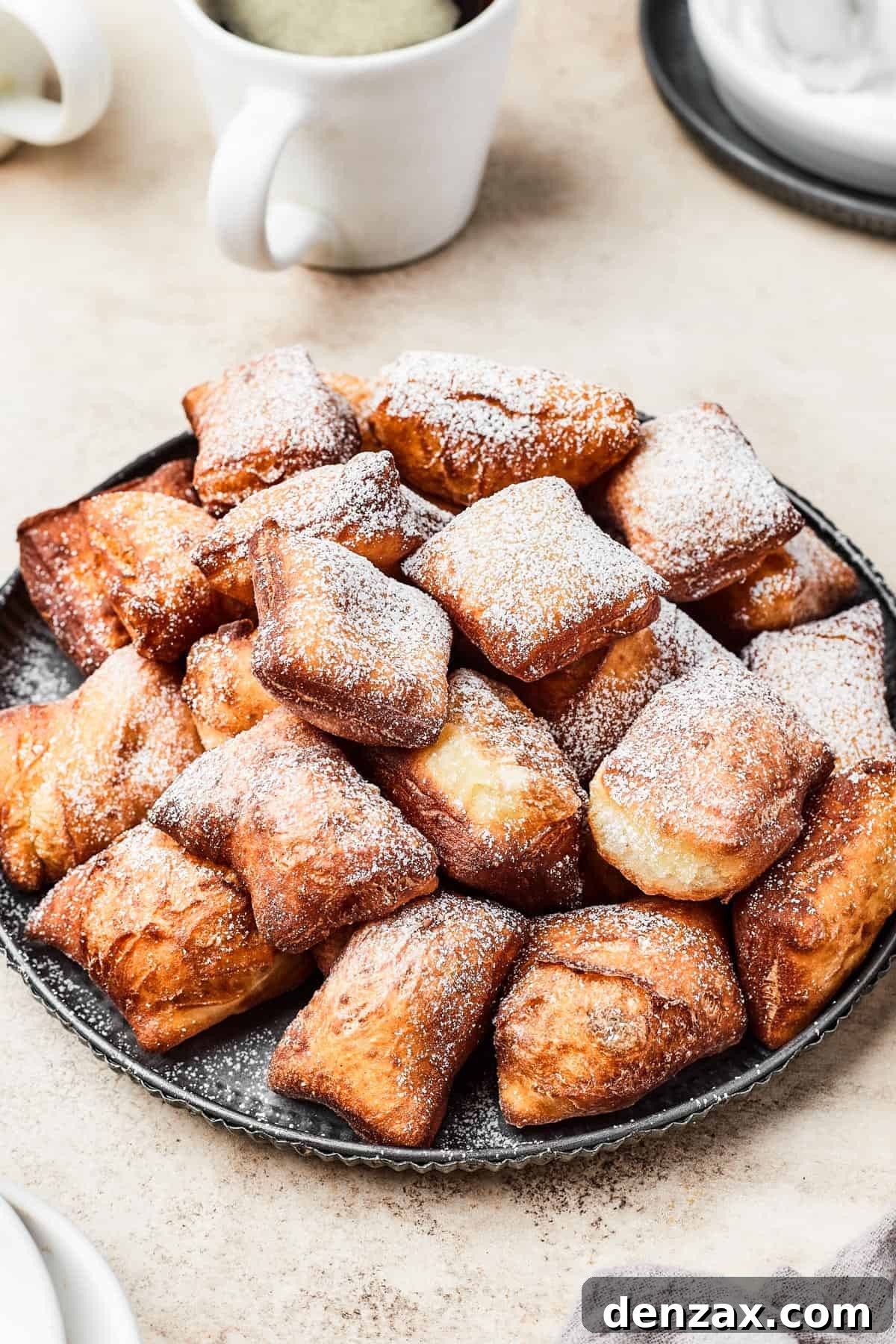 A plate of freshly fried beignets, generously dusted with powdered sugar, ready to be enjoyed.