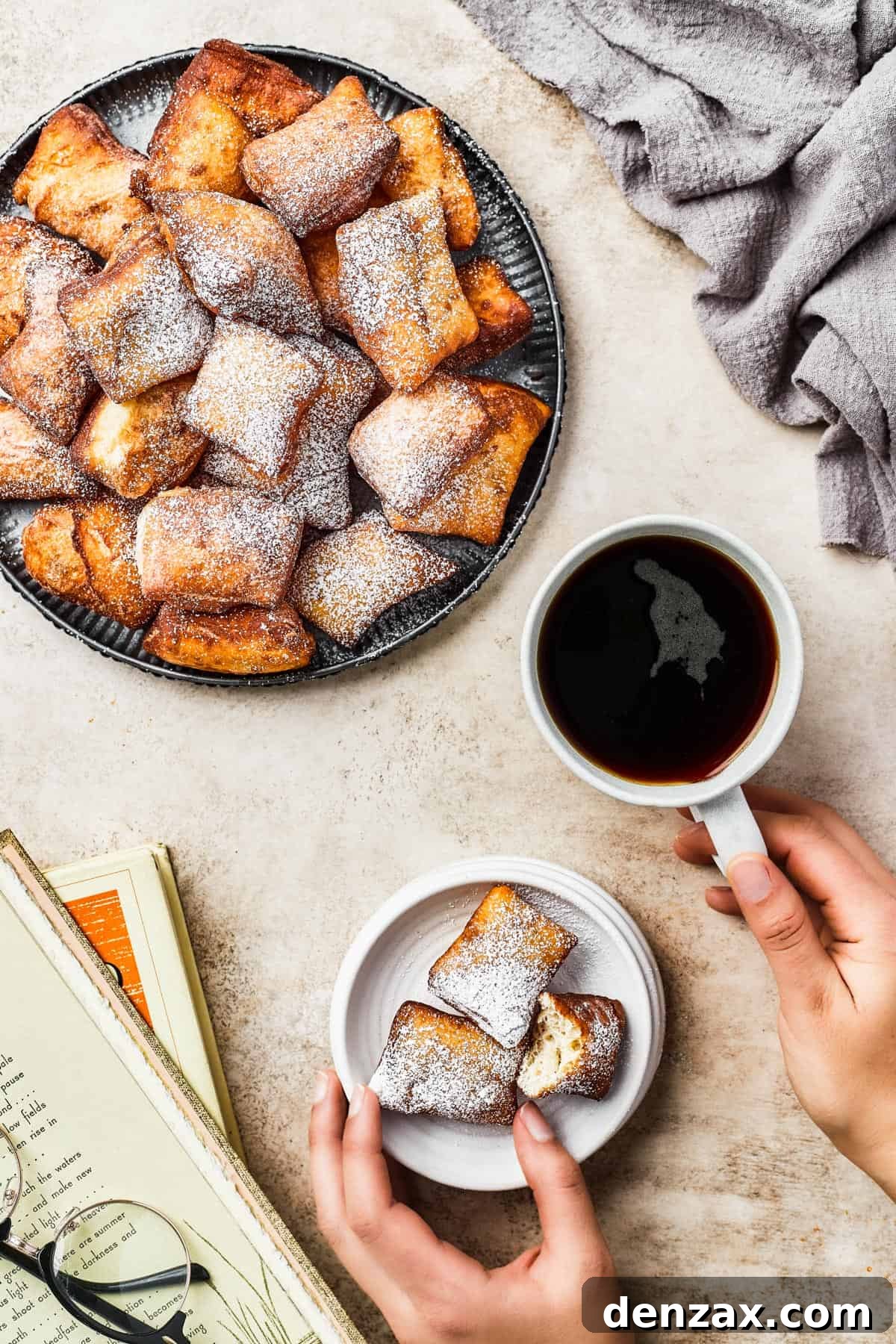 An inviting overhead shot of a large platter overflowing with golden-brown beignets. A cup of dark coffee and a small serving of beignets are artfully placed nearby, suggesting a perfect pairing.