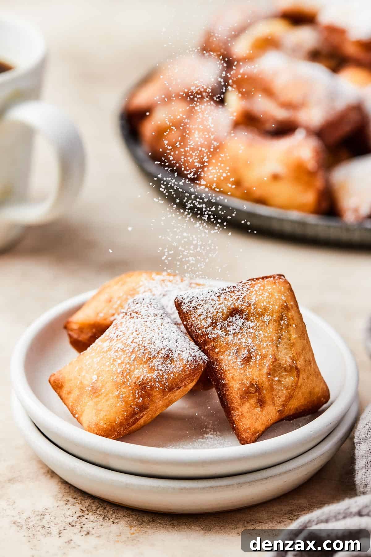 A close-up shot capturing the moment powdered sugar is delicately sprinkled over three freshly fried beignets, arranged on pristine white plates, highlighting the finishing touch.
