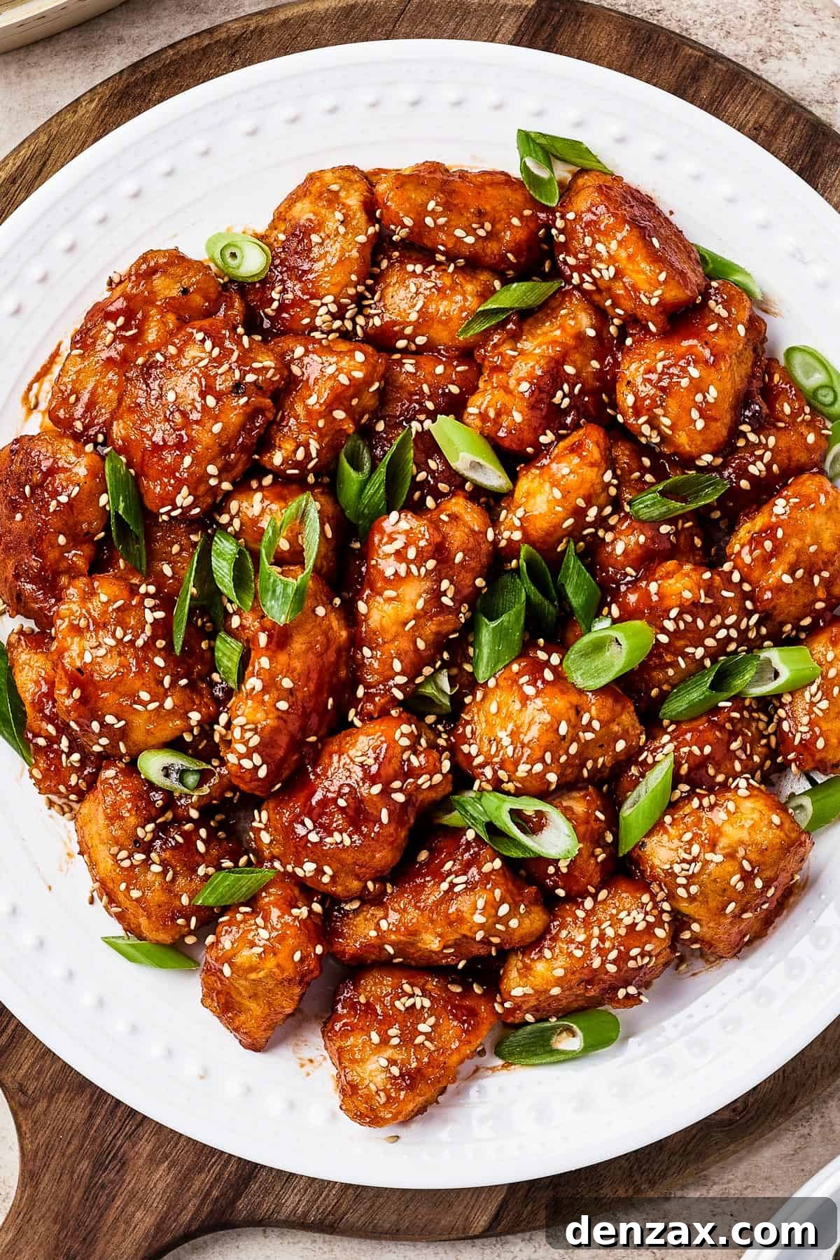 A close-up shot of a serving of homemade sweet and sour chicken, garnished with green onions and sesame seeds, alongside fluffy white rice.