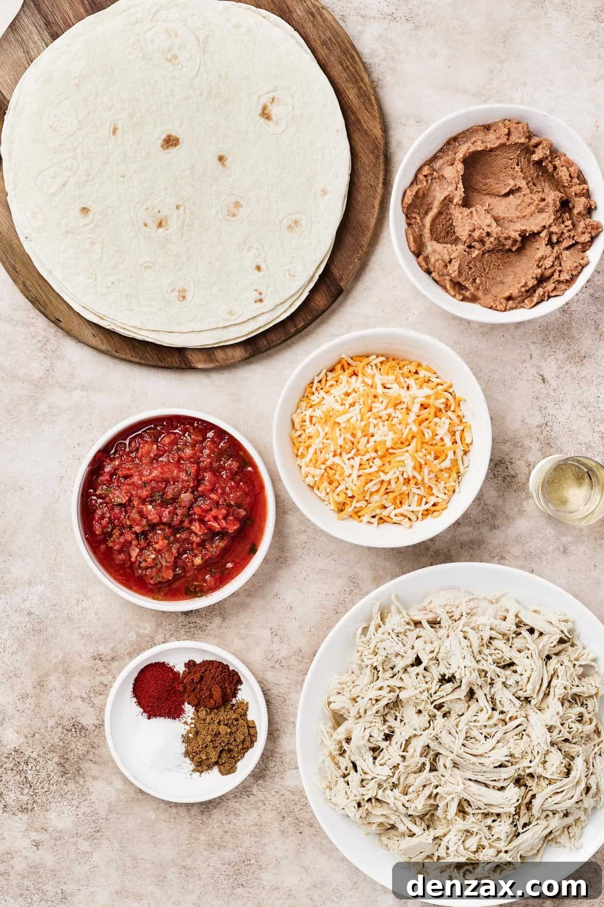 Individual ingredients for chicken chimichangas laid out: large flour tortillas, canned refried beans, a bowl of salsa, shredded Mexican blend cheese, cooking oil, spices, and a bowl of shredded cooked chicken.