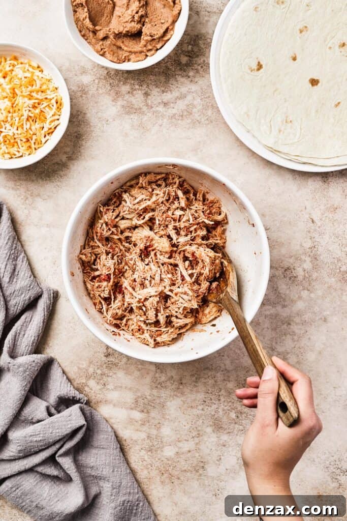 Shredded cooked chicken mixed thoroughly with salsa and Tex-Mex spices in a white mixing bowl, ready for chimichanga assembly.