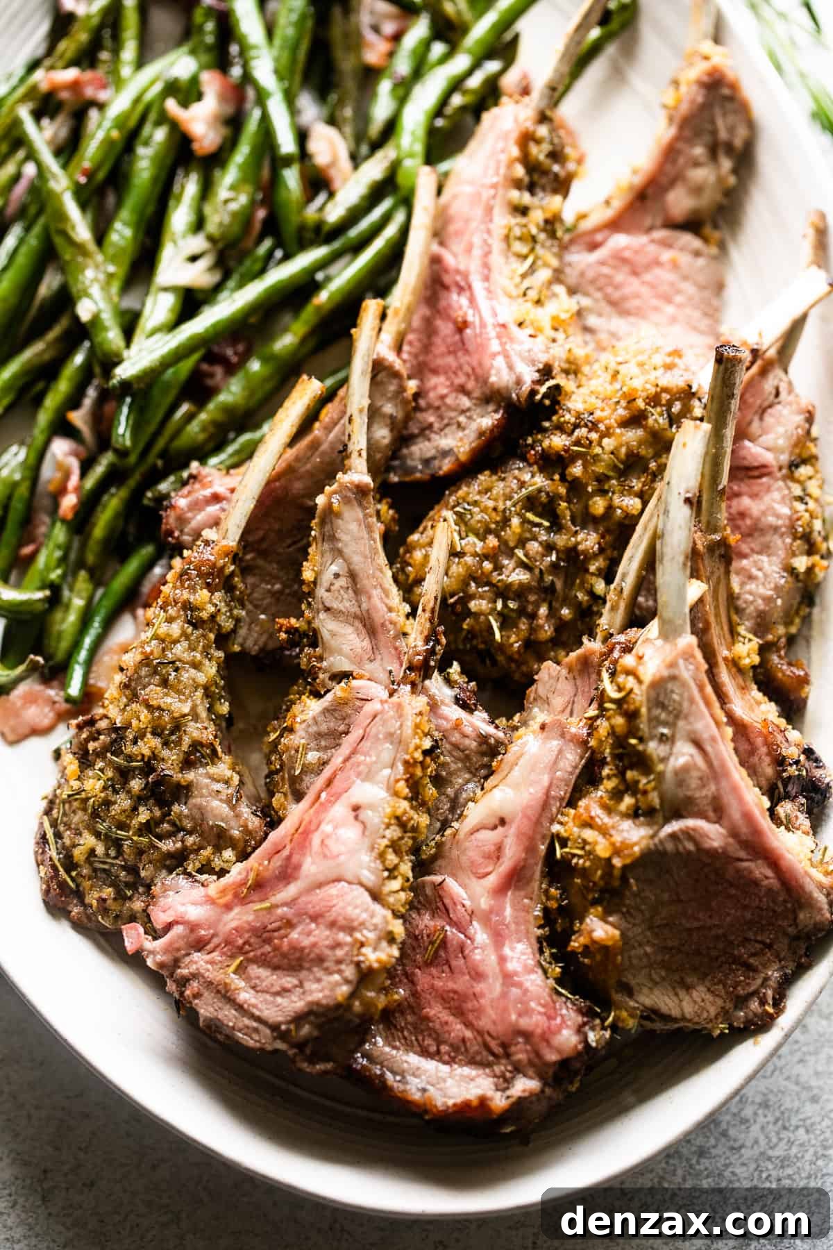up close shot of breadcrumb coated lamb chops arranged on a serving platter with a side of green beans placed above the chops.
