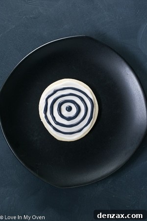 Step-by-step image showing a toothpick dragging through the black icing to create the web effect.