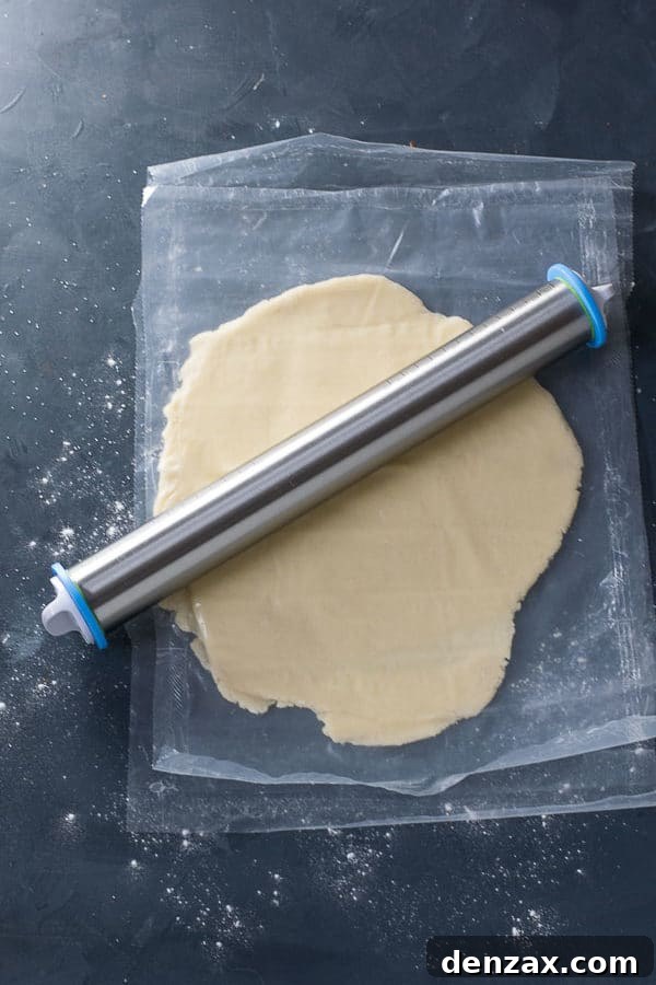 An adjustable rolling pin rolling out cookie dough between two sheets of parchment paper.