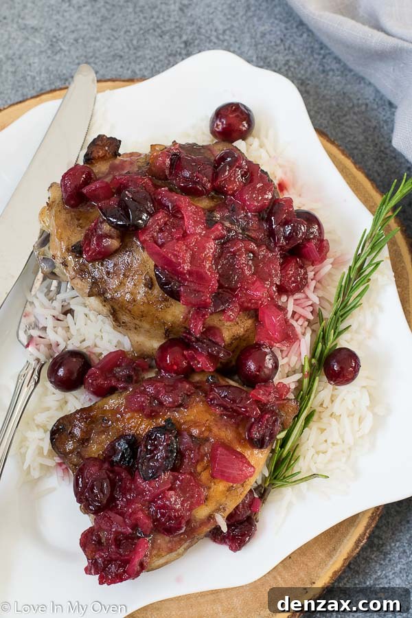 Cranberry Chicken Thighs on a plate with rice and green vegetables, garnished with fresh cranberries.