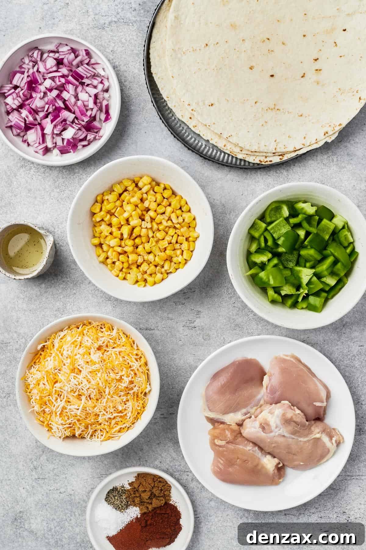 Ingredients for chicken quesadillas laid out: red onion, tortillas, olive oil, corn kernels, bell pepper, shredded cheese, chicken thighs, and a bowl of spices.