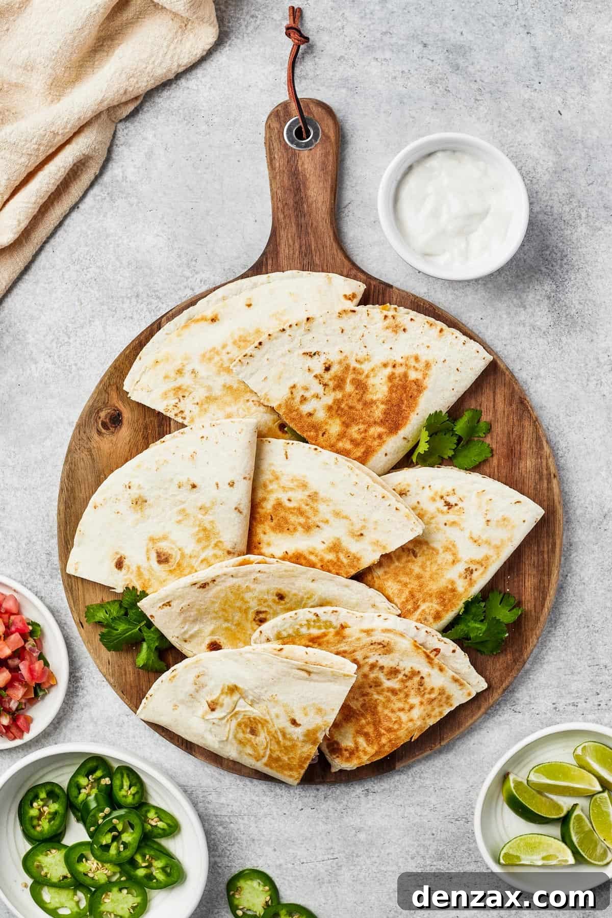 Two halves of a chicken quesadilla, expertly cut and fanned out on a wooden board, garnished with a vibrant sprig of cilantro and a fresh jalapeno slice.