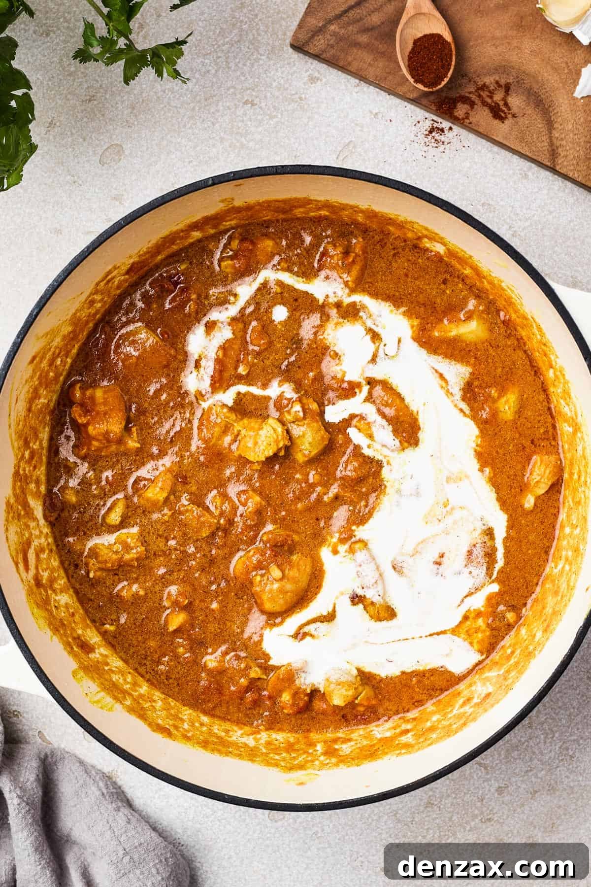 Butter Chicken Makhani 4 Heavy pot with chicken simmering in tomato sauce, with cream being added.