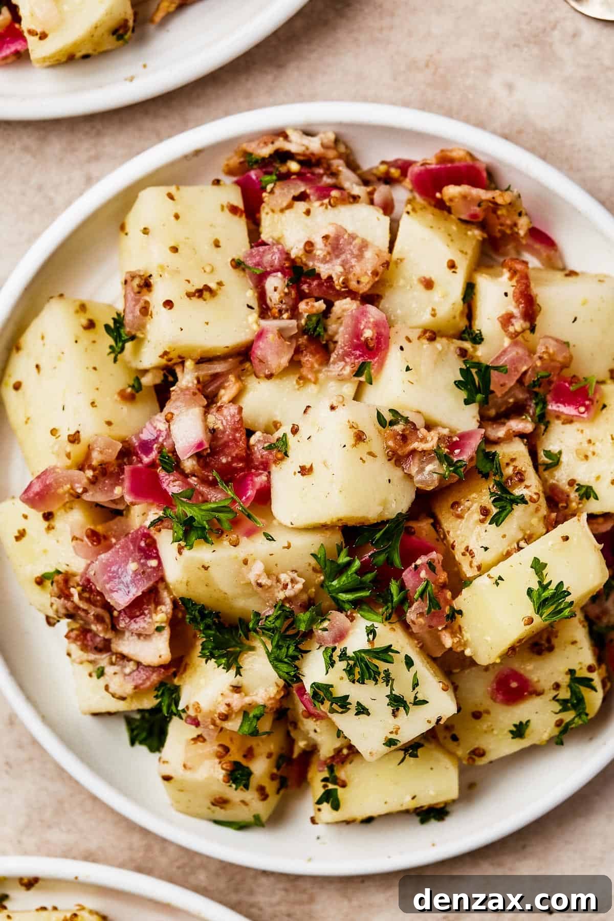 Overhead shot of several small plates, each with a serving of warm German potato salad in bacon dressing, ready to be enjoyed.