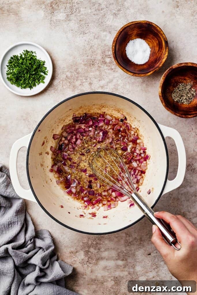 Chopped red onion and minced garlic cooking in a pot with bacon grease, forming the aromatic base of the dressing.