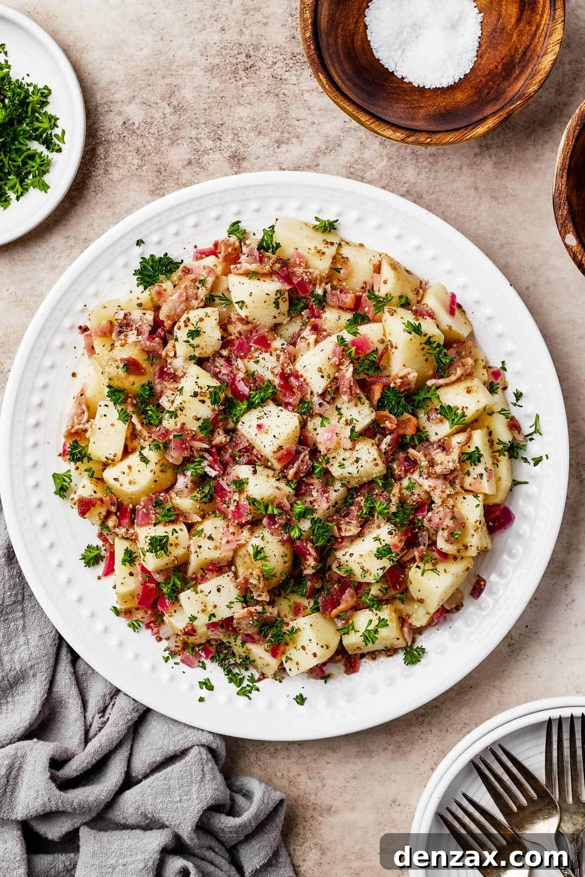 A plate of warm German potato salad garnished with fresh herbs and crispy bacon, showcasing its appetizing appeal.