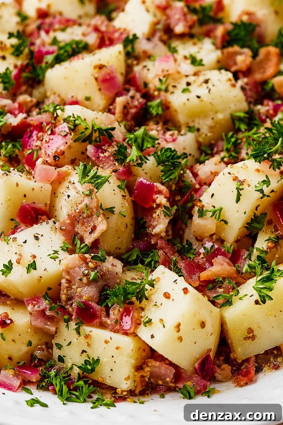 Close-up shot of warm German potato salad on a white serving dish, highlighting its texture and inviting presentation.