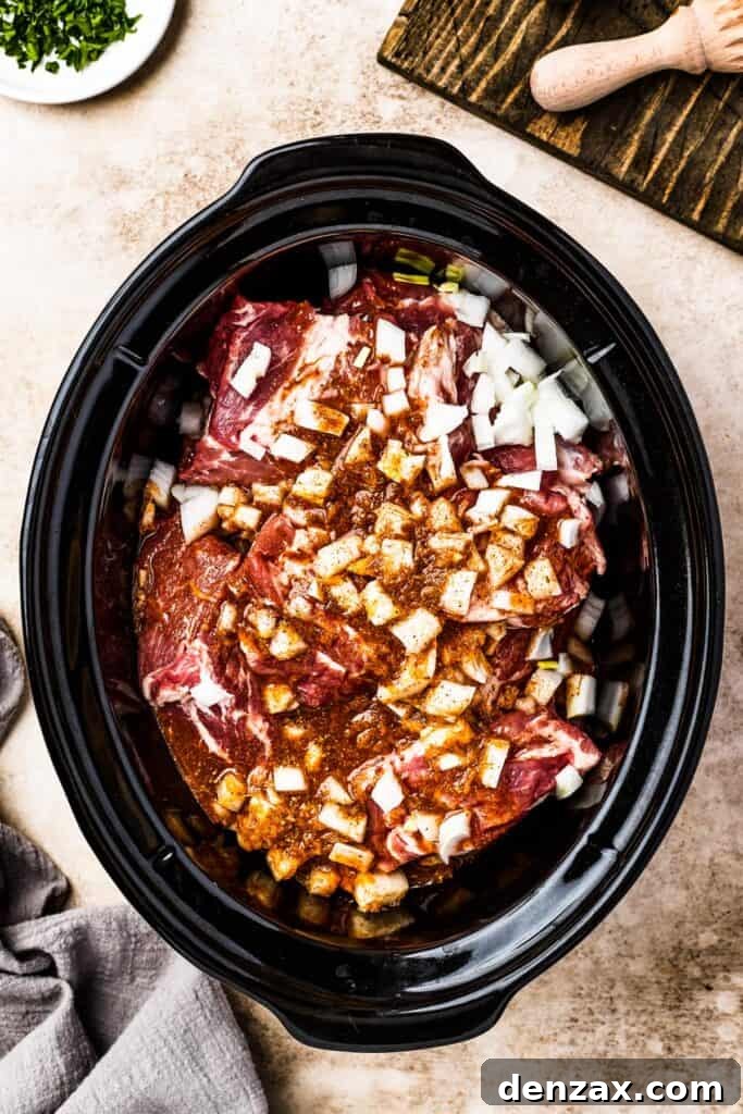 Chunks of pork and diced onion nestled in a slow cooker, topped with the fragrant spiced liquid.
