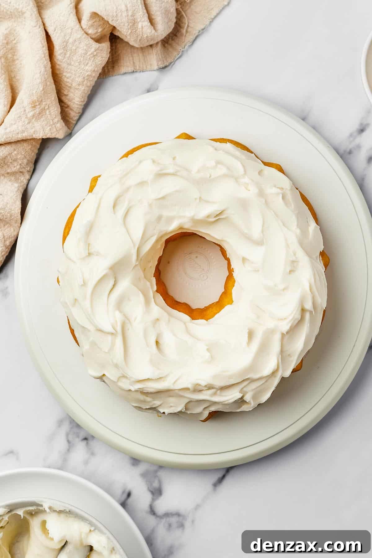 A perfectly frosted bundt cake adorned with thick, creamy cream cheese frosting, hinting at its rich texture and tangy flavor. A bowl of freshly made frosting and a dish of bright lemon zest sit nearby, suggesting fresh ingredients and homemade goodness.