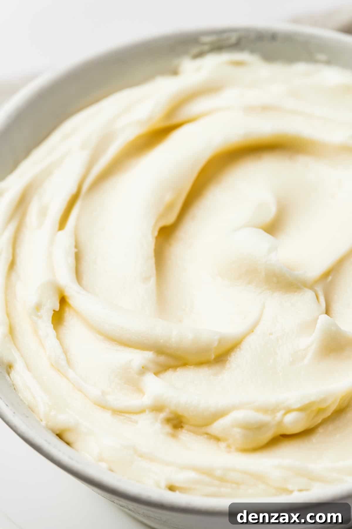 A close-up shot revealing the incredibly smooth, thick, and fluffy texture of homemade cream cheese frosting, swirled invitingly in a large mixing bowl.