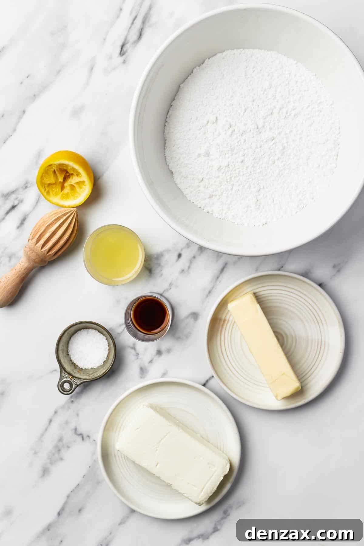 Six essential ingredients for cream cheese frosting laid out: powdered sugar, softened butter, pure vanilla extract, a pinch of salt, a block of full-fat cream cheese, and white vinegar.