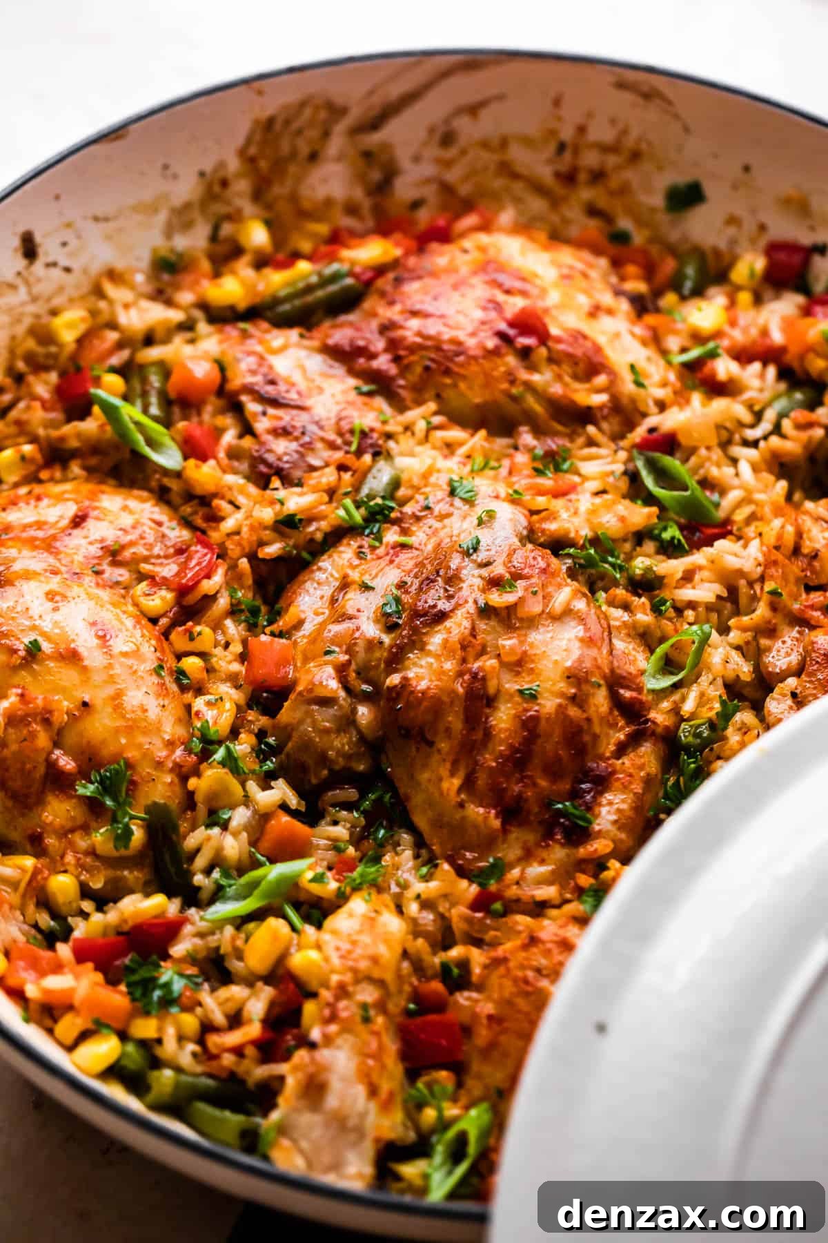 Side view of a serving of cooked ranch chicken thighs with fluffy rice and colorful mixed vegetables in a skillet.