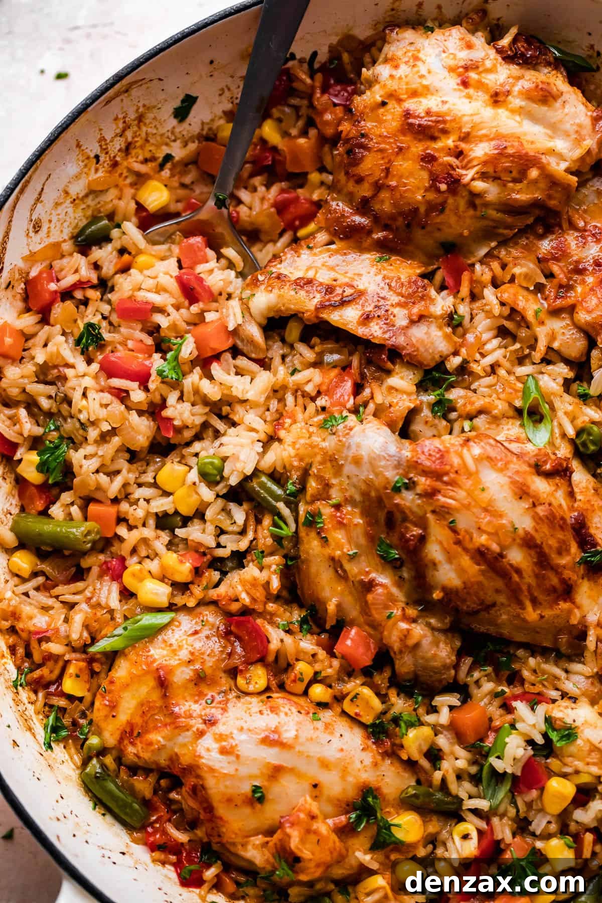 Close-up overhead shot of a round casserole dish with cooked ranch chicken thighs, rice, and mixed vegetables, ready to be served.
