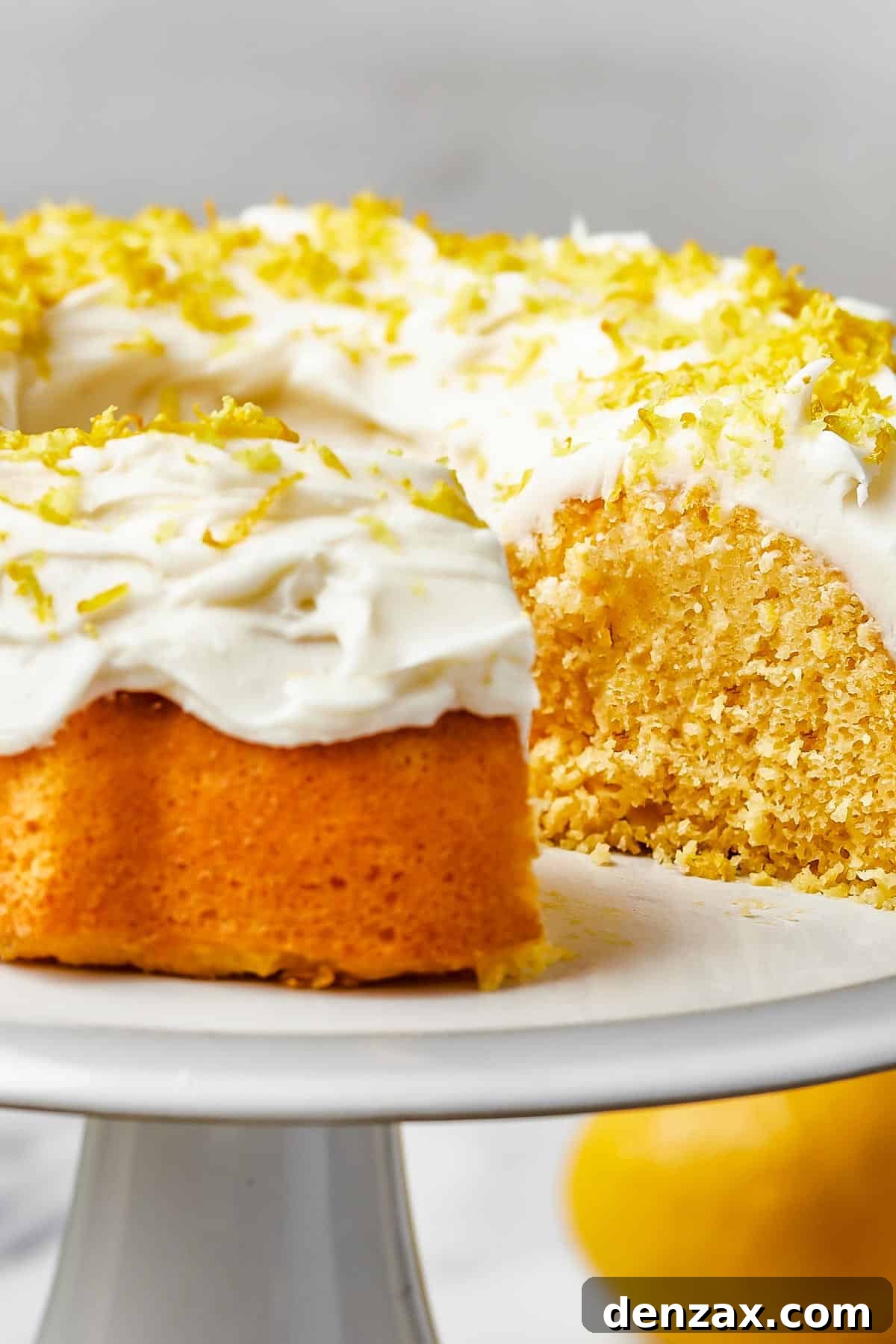 A close-up of a generously frosted Lemon Bundt Cake, adorned with bright yellow lemon zest, ready to be sliced.