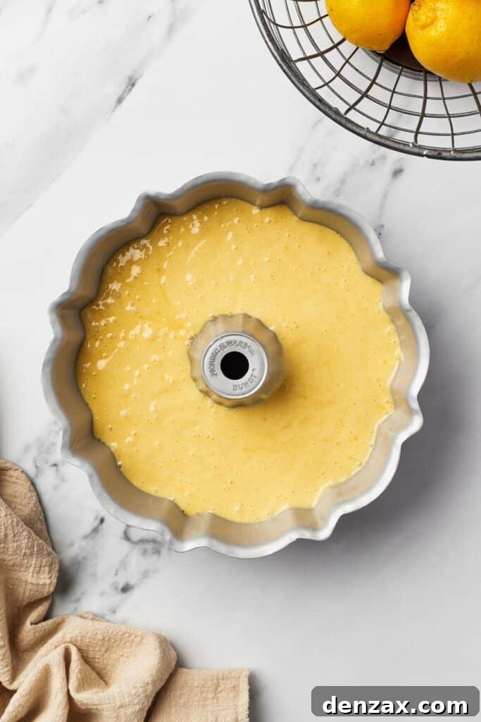 A Bundt pan, meticulously greased and ready, now filled with smooth, vibrant yellow lemon cake batter.
