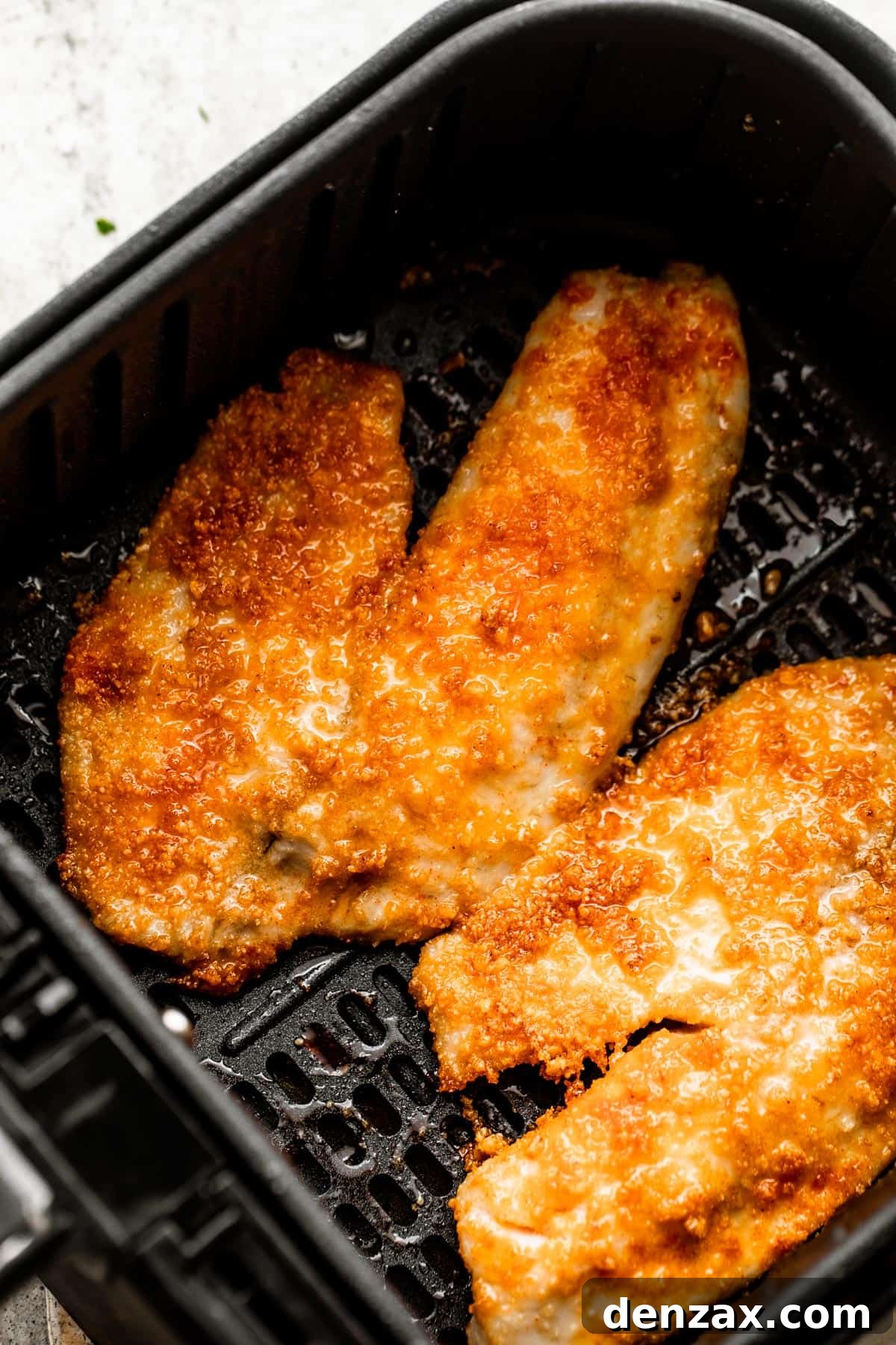two cooked tilapia fillets arranged inside of a black air fryer basket.