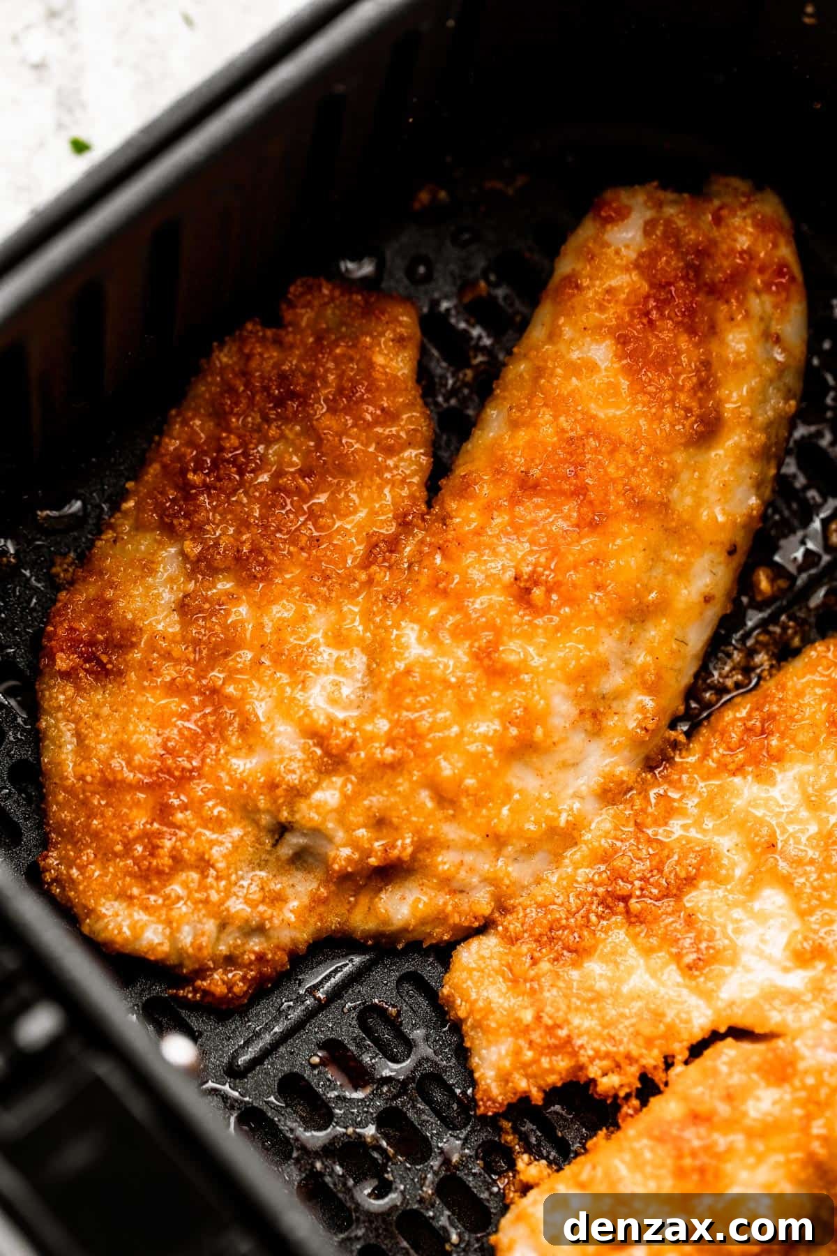 two cooked tilapia fillets arranged inside of a black air fryer basket.