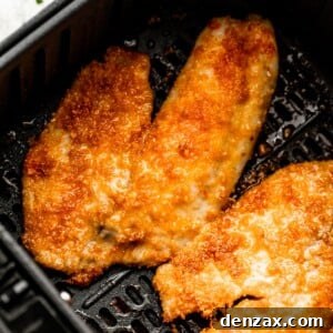 two cooked tilapia fillets arranged inside of a black air fryer basket.
