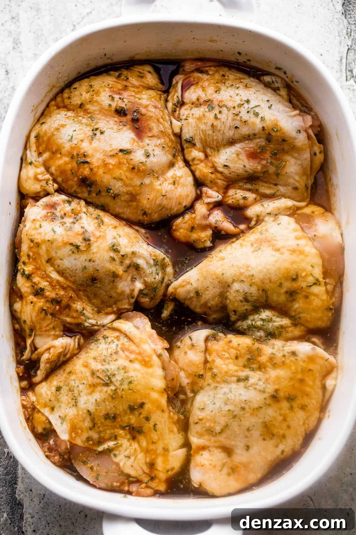 Overhead image of a white baking dish with six raw bone-in, skin-on chicken thighs arranged inside of the baking dish.