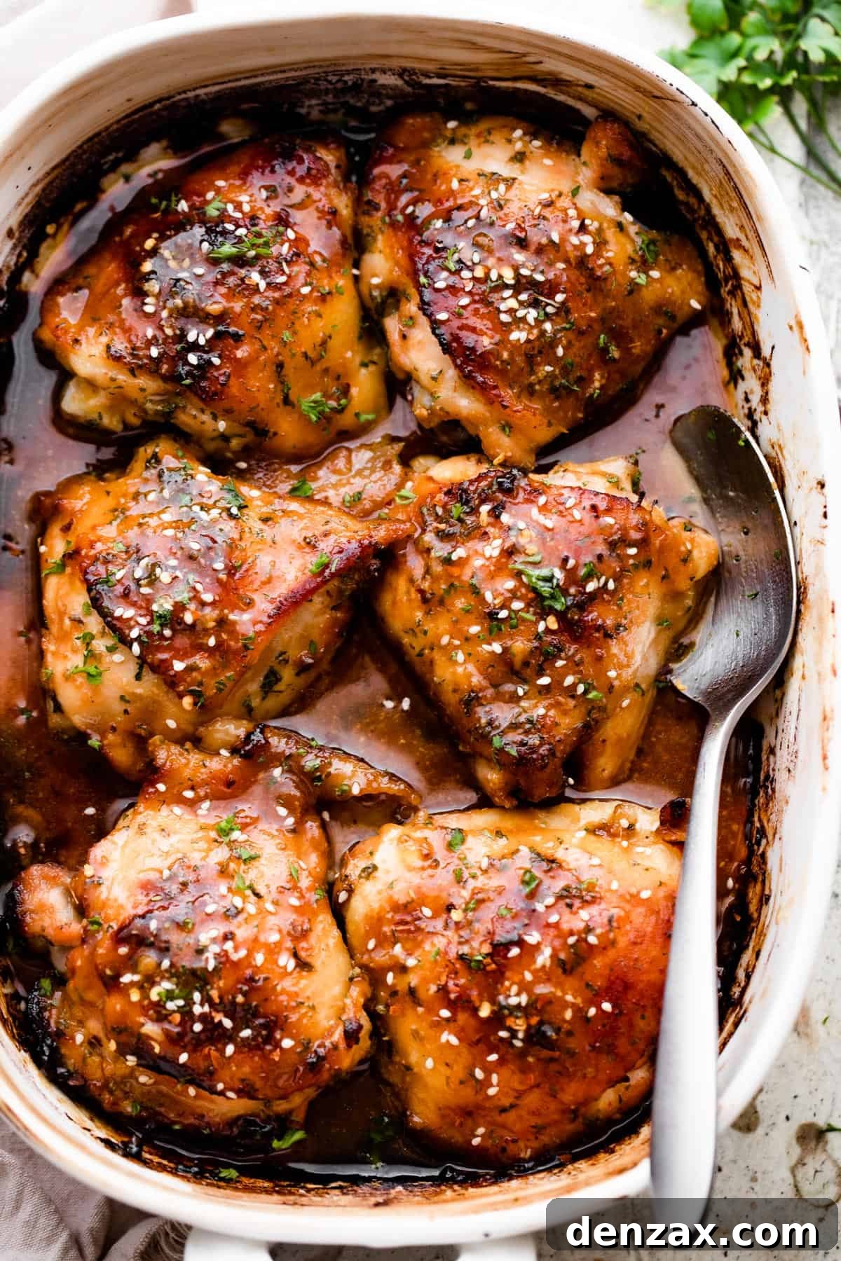 Overhead shot of a baking dish with six honey garlic baked chicken thighs garnished with sesame seeds.