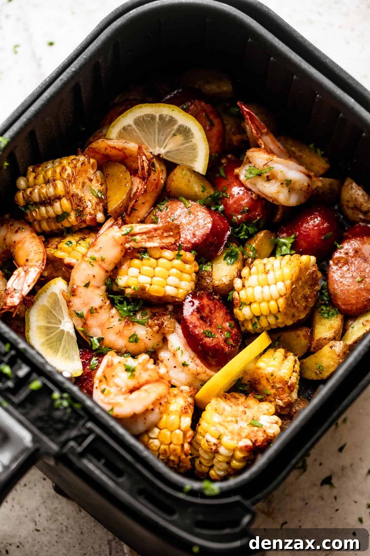 Overhead view of a colorful assortment of corn rounds, flavorful andouille sausage slices, plump shrimp, and bright lemon wedges arranged inside an air fryer basket, ready for cooking.
