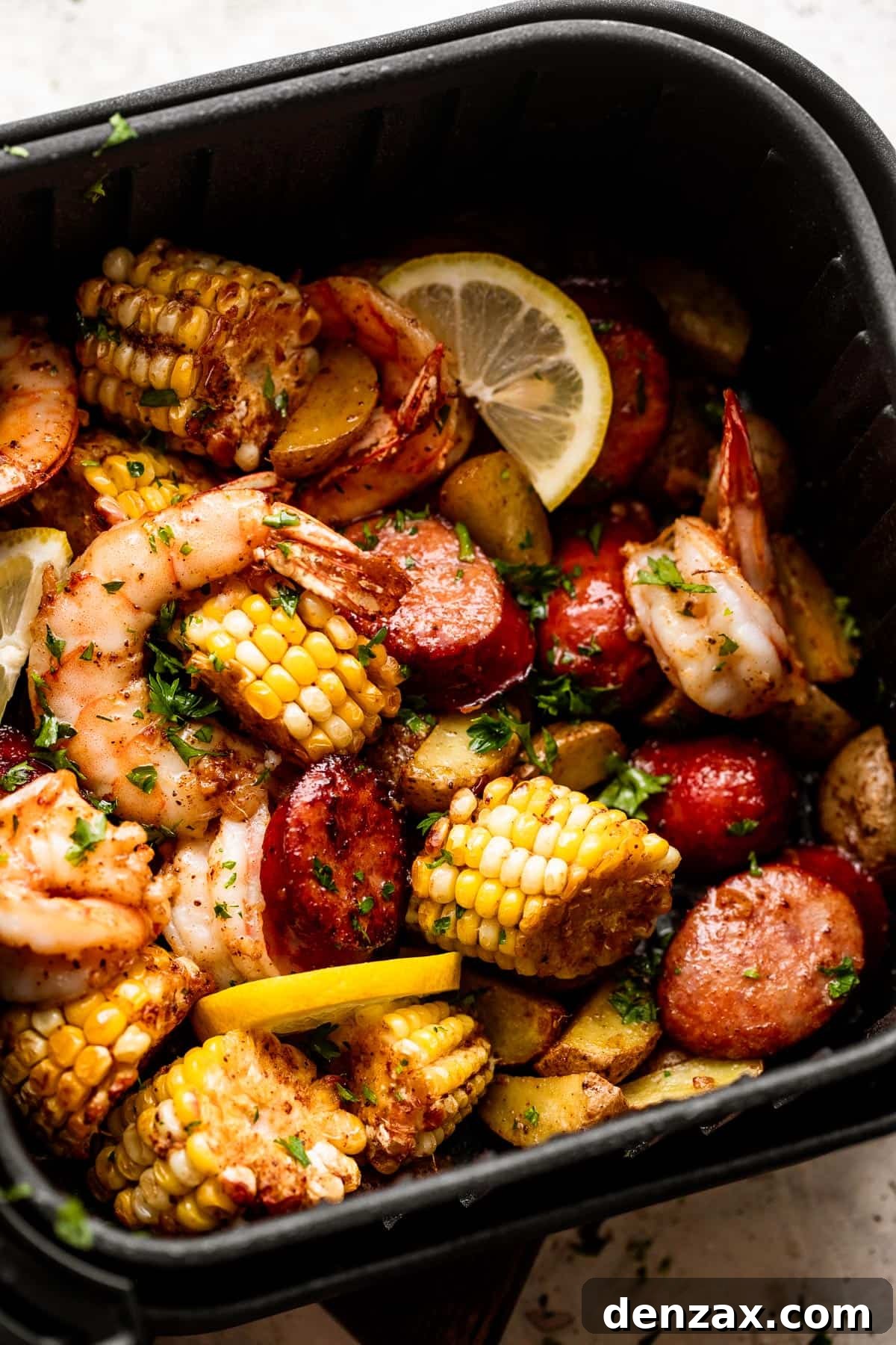 Close-up overhead shot of the delicious Air Fryer Shrimp Boil in a black air fryer basket, featuring succulent shrimp, spicy andouille sausage, sweet corn, and tender potatoes, garnished with lemon slices.