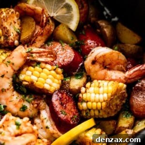 Close-up shot of corn on the cob rounds, andouille sausage rounds, shrimp, and lemon slices inside of a black air fryer basket.