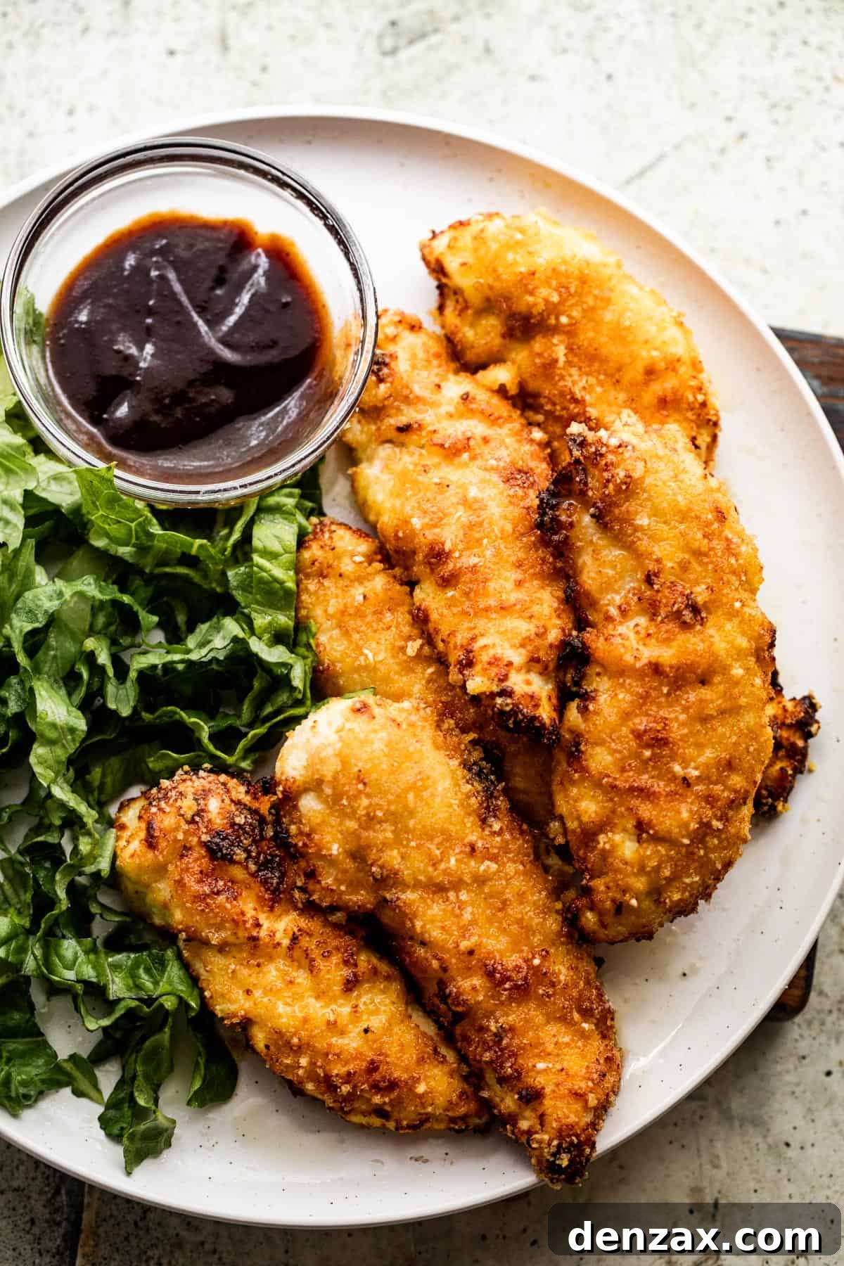Overhead shot of a dinner plate with crispy air fryer chicken tenders, fresh greens, and a side of savory BBQ sauce.
