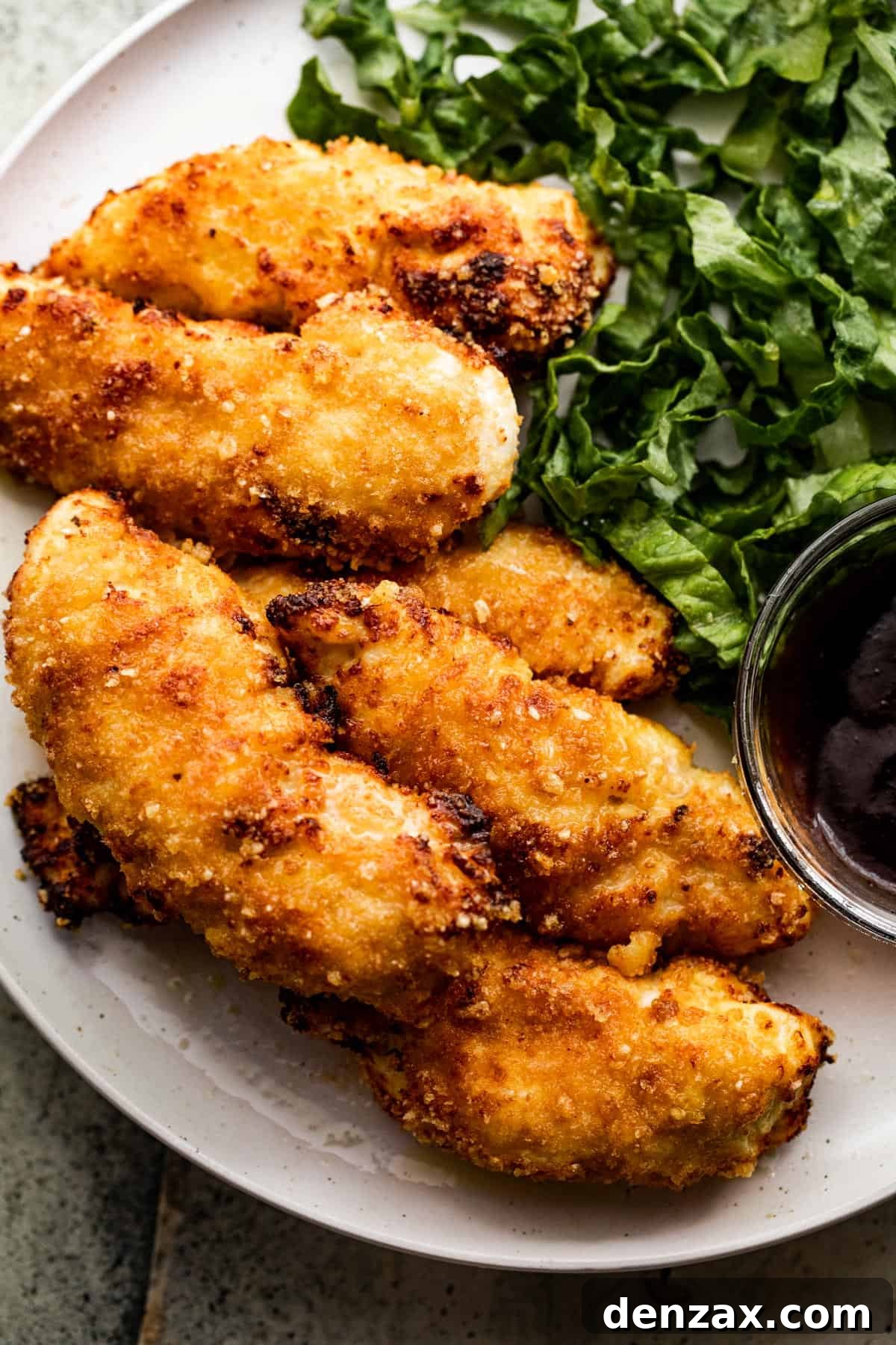 Close-up overhead shot of a dinner plate showcasing golden air fryer chicken tenders, a vibrant green salad, and a dollop of barbecue sauce.