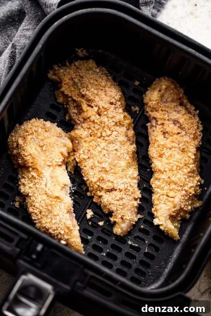 Three raw breaded chicken tenders carefully arranged inside a black air fryer basket, ready for cooking.