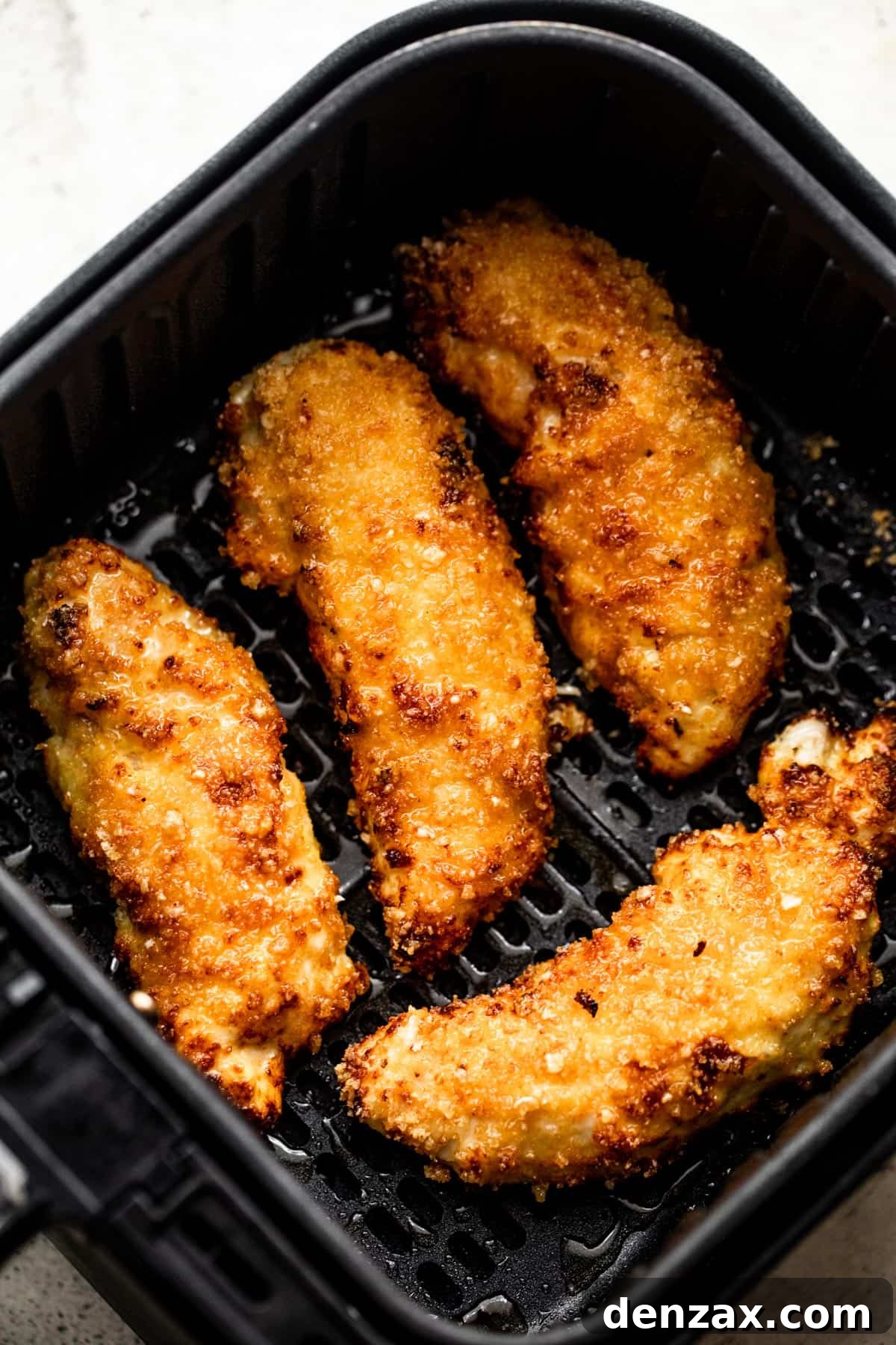 Four breaded and perfectly cooked chicken tenders nestled inside a black air fryer basket, ready to be served.