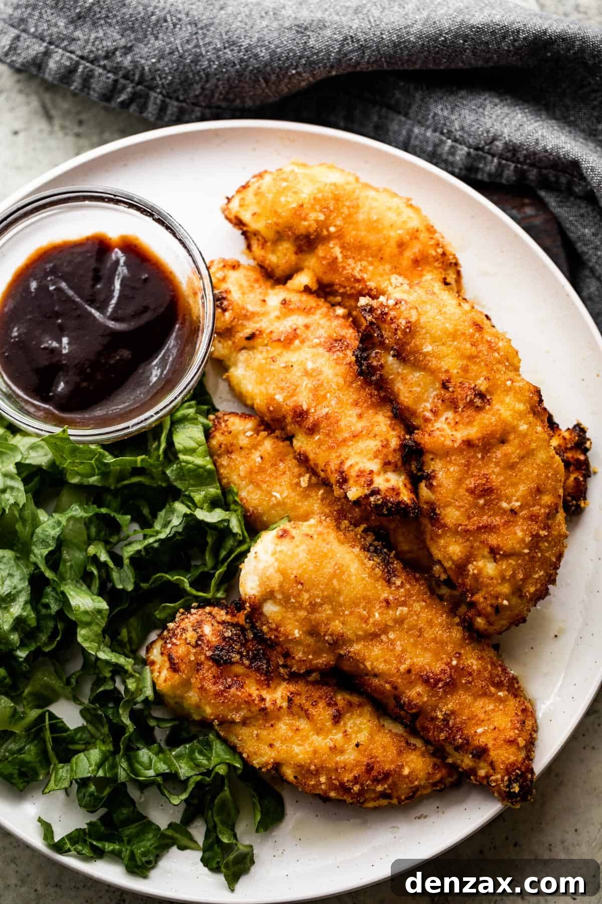 A beautifully plated dinner featuring golden air fryer chicken tenders, a fresh green salad, and a side of savory BBQ dipping sauce.
