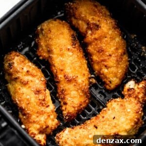 Four breaded and cooked chicken tenders arranged inside a black air fryer basket.