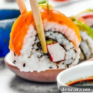 A bite of sushi held in a pair of chopsticks. A small plate of sushi and a container of soy sauce is in the background.