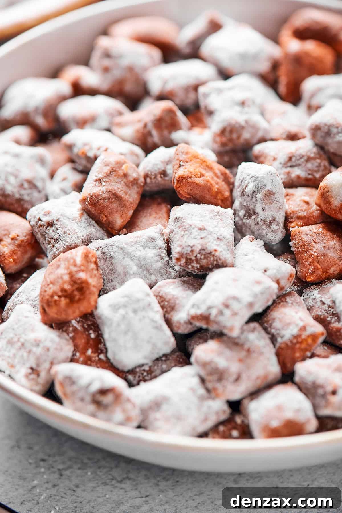 Puppy Chow 4 Close-up shot of puppy chow in a white bowl, to show the texture. Some pieces are fully coated in powdered sugar, while others are not.