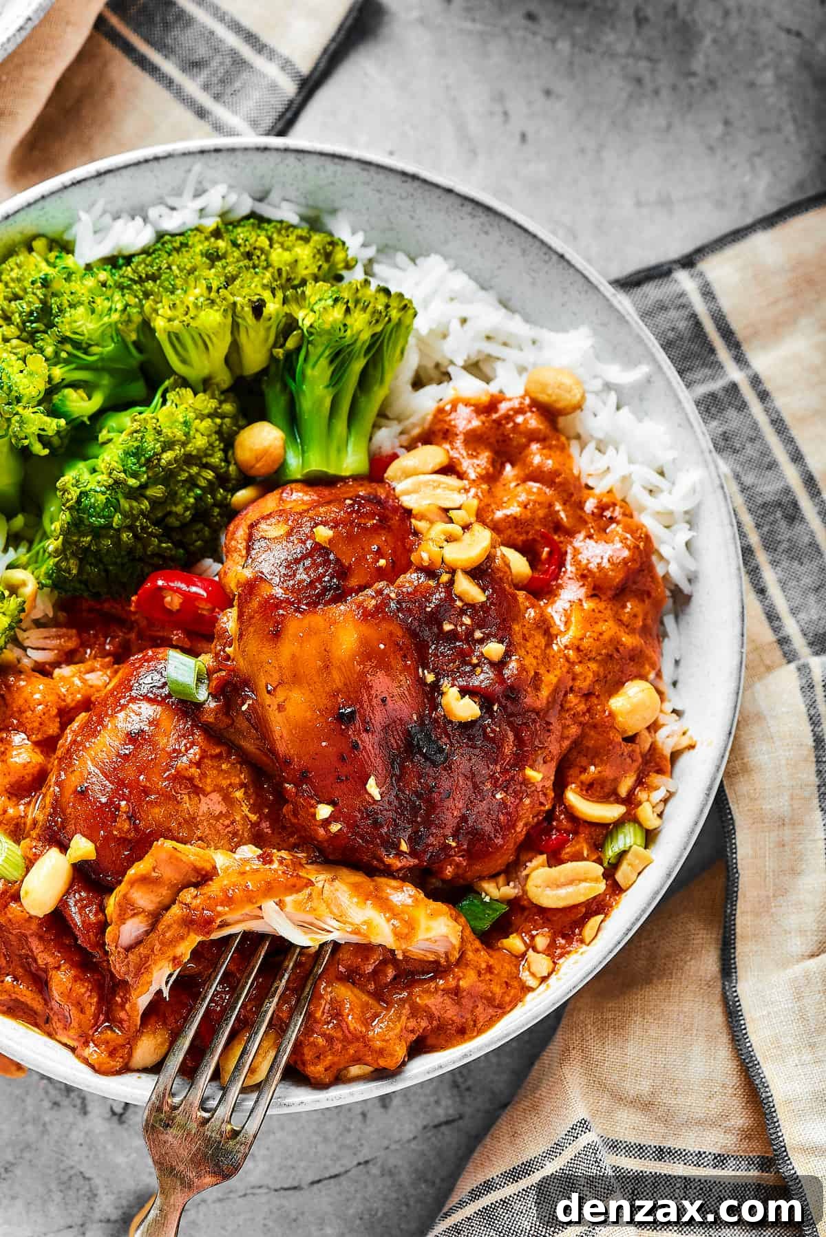 overhead shot of a chicken thigh cooked in peanut sauce, with a fork pulling away a bite.