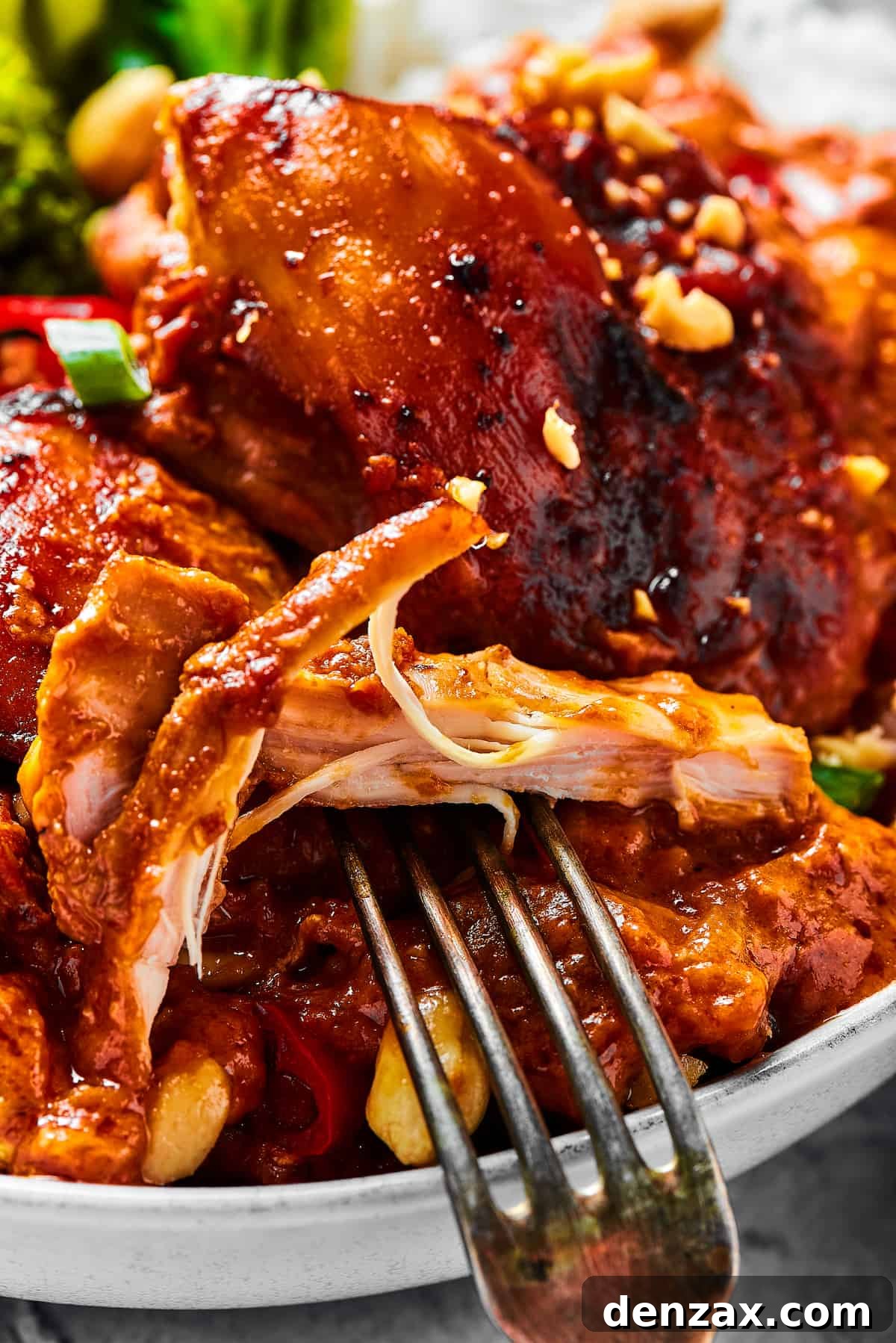 A close-up shot of a chicken thigh cooked in peanut sauce, with a fork pulling away a bite.